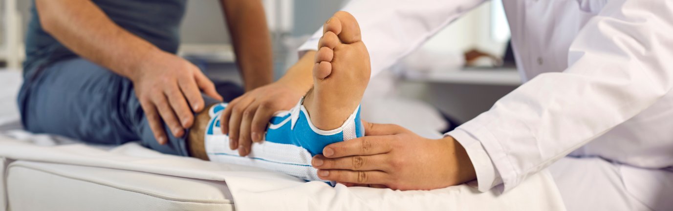 Durante una visita ortopedica il medico controlla e sostiene un piede ingessato di un paziente
